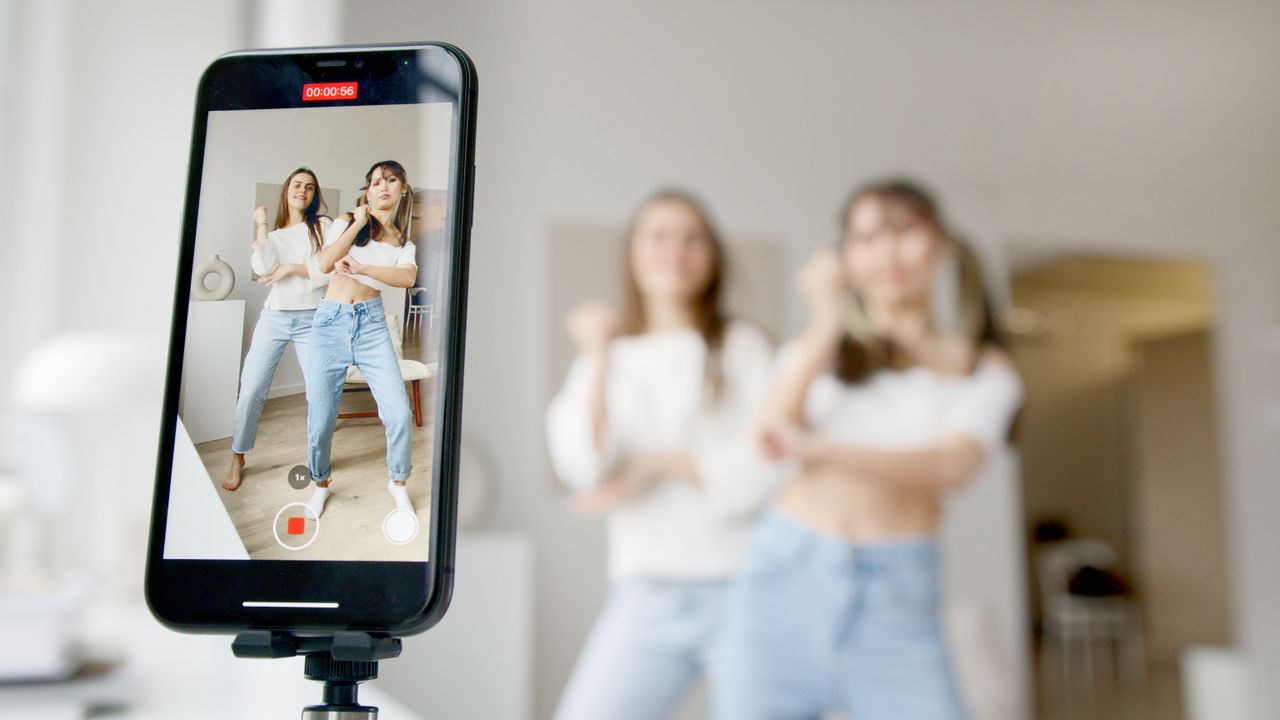 services-02 Two women dance in front of a smartphone camera, recording content indoors.
